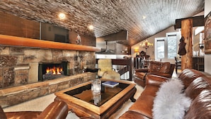 A cozy living room with a stone fireplace, leather furniture, and a rustic ceiling.