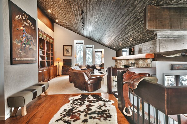 A spacious living room with a wooden ceiling, leather furniture, a large rug, and a mounted saddle.