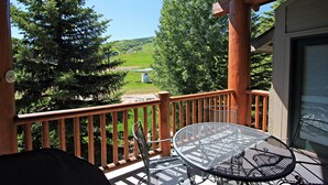 A balcony with a metal table and chairs, overlooking a green landscape with trees and a distant building. - Snow Flower 076 4 Bedroom Condo by RedAwning (Park City)