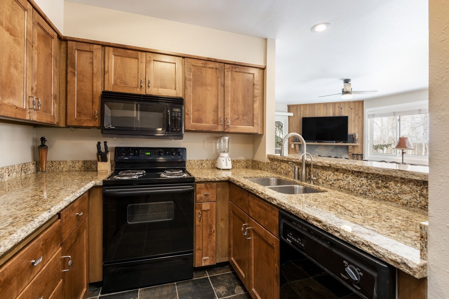 A kitchen with wooden cabinets, a black stove, a microwave, a sink, and a dishwasher.