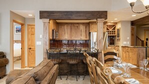Una cocina con armarios de madera, una isla central con taburetes y un comedor con mesa de madera dispuesta para cuatro.