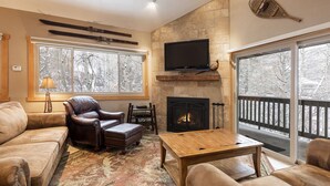 Un salón acogedor con chimenea, sillón de cuero y un ventanal con vistas nevadas.