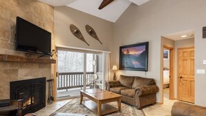 Una sala de estar acogedora con chimenea, muebles de cuero, un televisor de pantalla plana y un ventanal con vistas a una terraza.