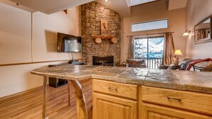 A modern kitchen with a stone fireplace, wooden cabinets, and a large island.
