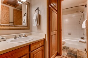 A bathroom with a wooden vanity, a sink, a mirror, and a shower area.
