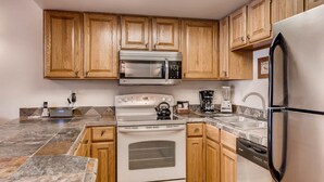 A modern kitchen with wooden cabinets, a stainless steel microwave, an oven, a dishwasher, and a refrigerator.