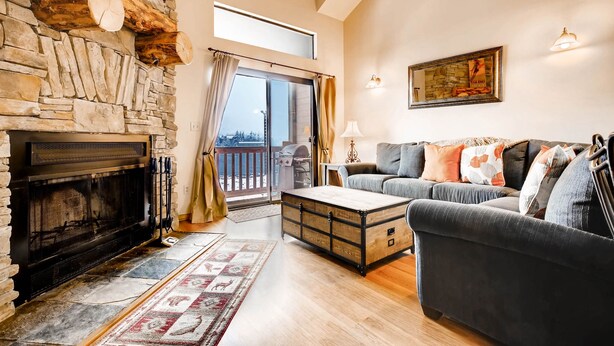 A living room with a stone fireplace, a sofa, a coffee table, and a view of the outdoors.