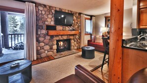 A cozy living room with a stone fireplace, a flat-screen TV mounted above it, and a comfortable seating area with a red couch and a round coffee table. - Snow Flower 003 2 Bedroom Condo by RedAwning (Park City)