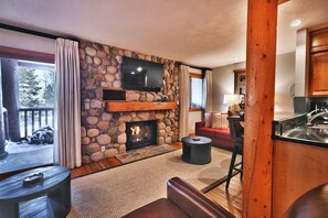 A cozy living room with a stone fireplace, a flat-screen TV mounted above it, a comfortable sofa, and a wooden coffee table.