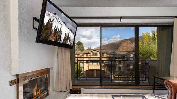 Una sala de estar moderna con chimenea, grandes puertas de vidrio correderas a un balcón y un televisor montado en la pared.