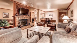 A spacious living room with a fireplace, comfortable seating, a flat-screen TV, and a dining area.