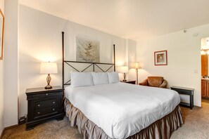 A neatly arranged bedroom with a large bed, two bedside tables with lamps, a chair, and a framed picture on the wall. - Park Station 218 2 Bedroom Condo by RedAwning (Park City)