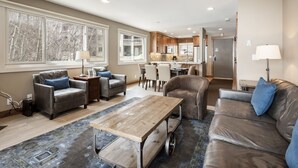 A spacious living room with leather sofas, a wooden coffee table, and a dining area with a kitchen in the background. - Snow Flower 120 2 Bedroom Condo by RedAwning (Park City)