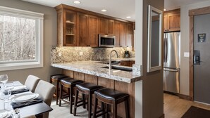 A modern kitchen with wooden cabinets, a stainless steel refrigerator, and a granite countertop. - Snow Flower 120 2 Bedroom Condo by RedAwning (Park City)