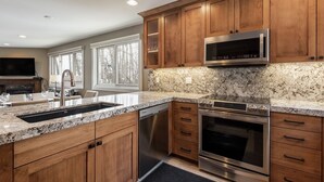 A modern kitchen with wooden cabinets, granite countertops, stainless steel appliances, and a large window providing natural light. - Snow Flower 120 2 Bedroom Condo by RedAwning (Park City)