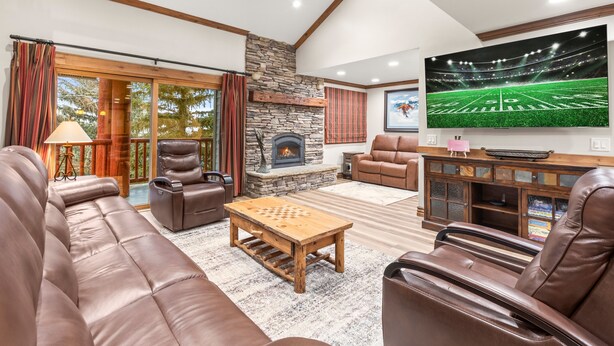 A spacious living room with leather sofas, a fireplace, a flat-screen TV, and a large window with curtains. - Snow Flower 071 3 Bedroom Condo by RedAwning (Park City)