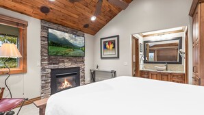 A bedroom with a stone fireplace, a bed, a ceiling fan, and a large window with a view of a mountain landscape. - Snow Flower 071 3 Bedroom Condo by RedAwning (Park City)