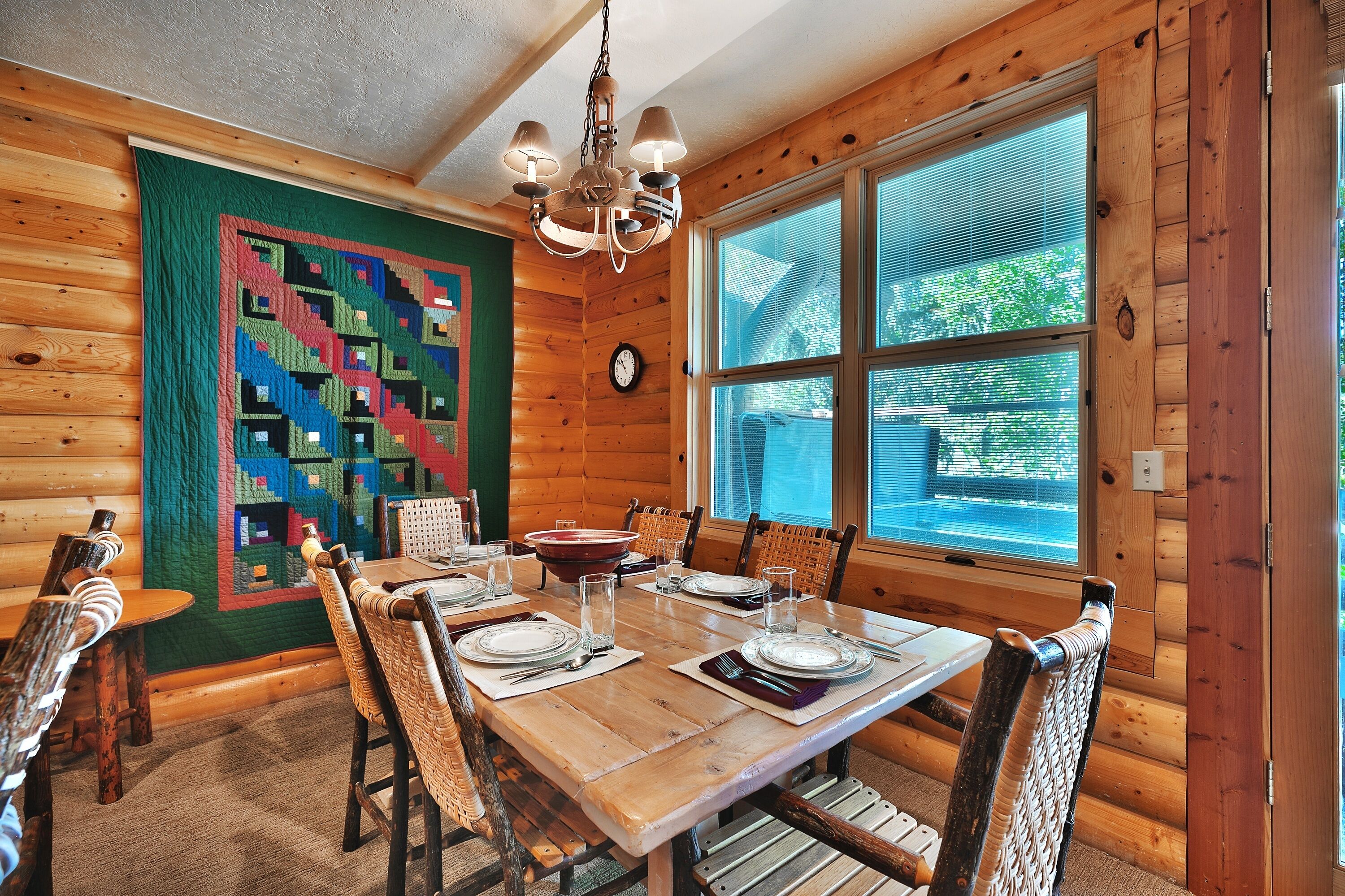 Comedor de una cabaña de madera con una gran mesa dispuesta para seis personas, rodeada de sillas de mimbre.