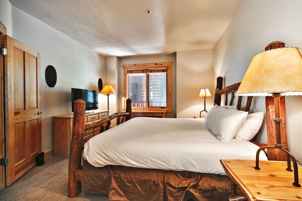 Un dormitorio con cama de madera, televisor, ventana con persianas y lámpara.