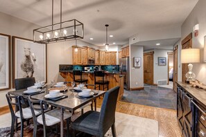 A modern kitchen with wooden cabinets, a central island, and a dining area with a table set for four. - Town Pointe C304 3 Bedroom Condo by RedAwning (Park City)