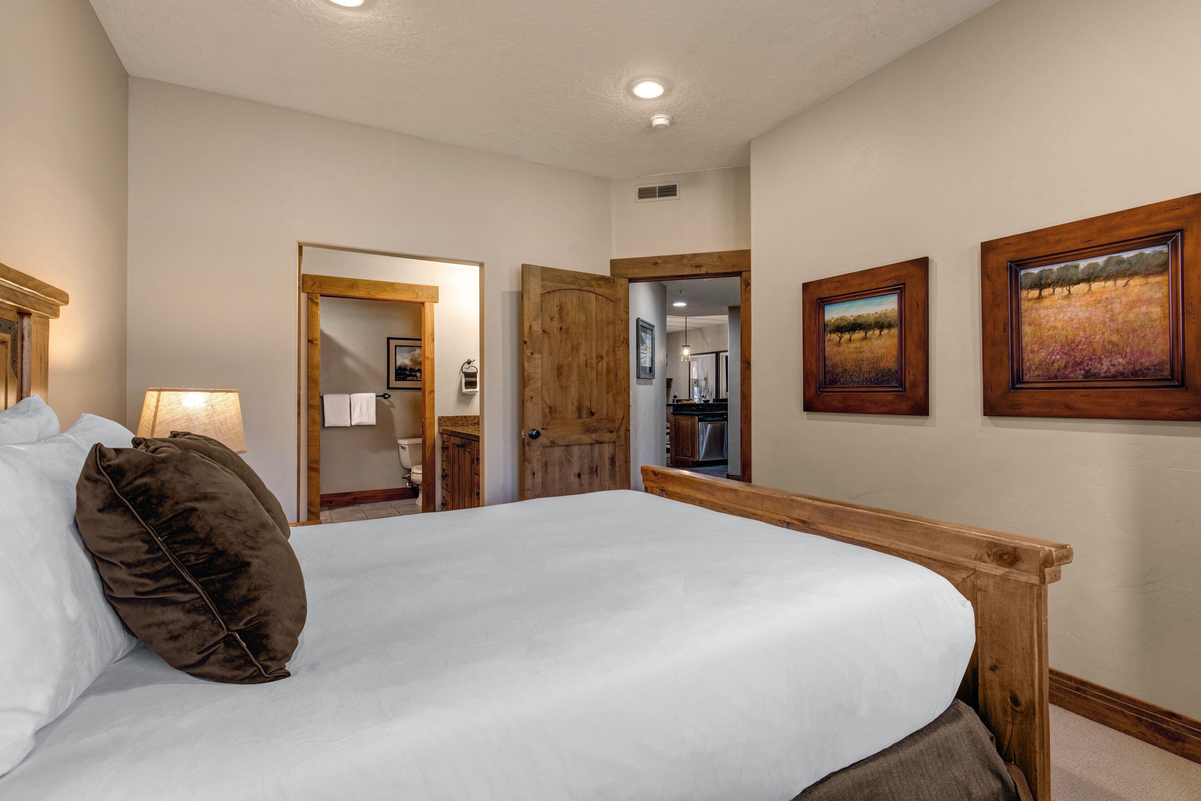 A bedroom with a large bed, wooden headboard, and two framed pictures on the wall.