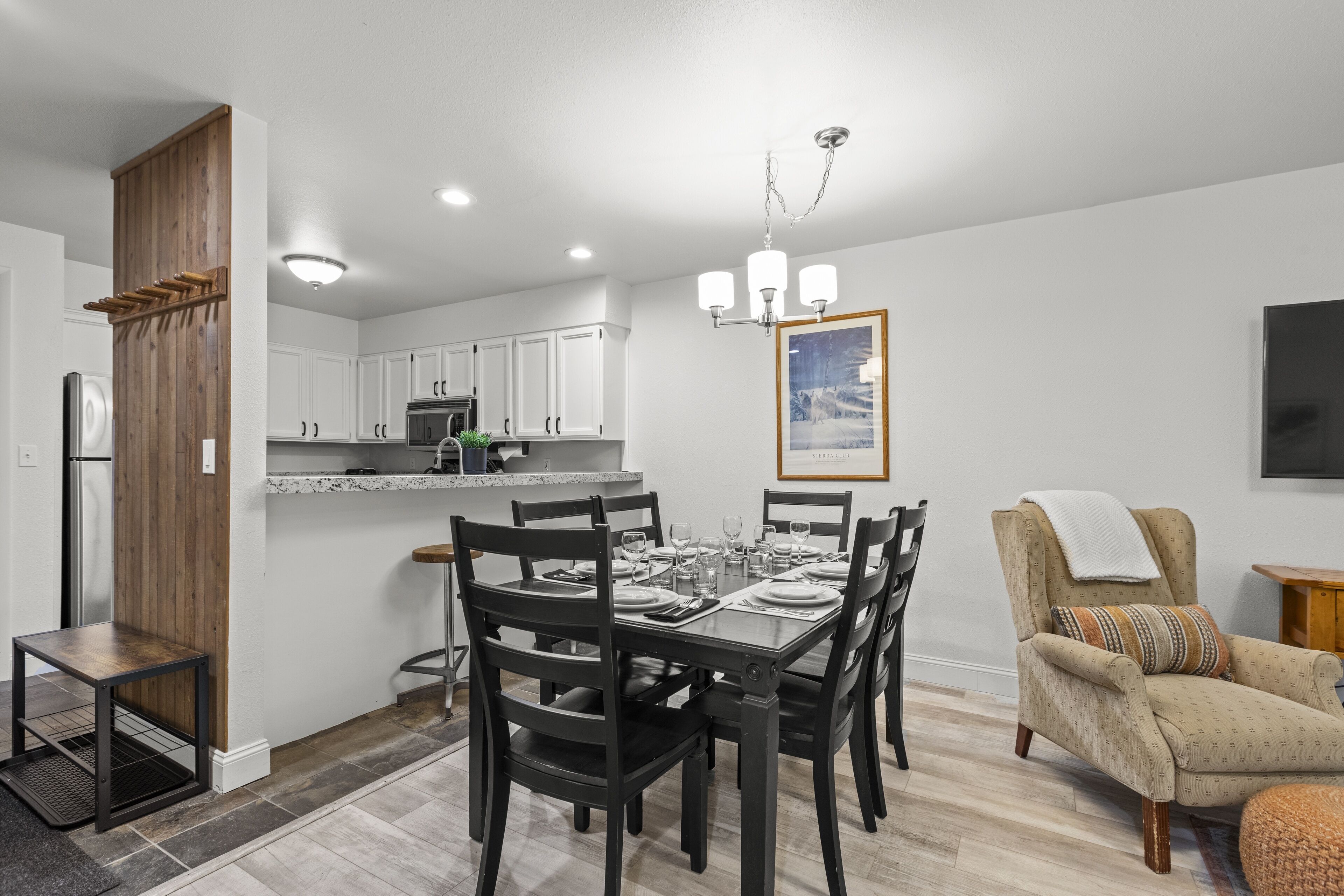 A modern kitchen with white cabinets, a dining table set for six, and a bar area with stools.