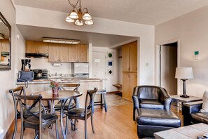 A modern kitchen with wooden cabinets, a dining area with a round table and chairs, and a leather armchair in a living area.