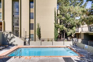 A swimming pool with a tiled deck, surrounded by a building with large windows and a staircase.
