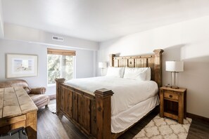 Um quarto com uma cama de madeira, uma mesa de cabeceira de madeira, um sofá de couro e um quadro na parede.