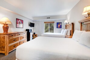 Habitación de hotel con dos camas, muebles de madera, televisión y obras de arte en las paredes.
