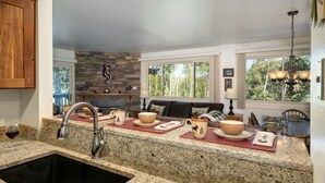 A kitchen with granite countertops, a stainless steel sink, a stone backsplash, and a dining area with a table and chairs. - Snow Flower 103 2 Bedroom Condo by RedAwning (Park City)