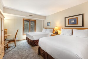 Una habitación de hotel con dos camas, un escritorio, una silla, un ventanal y un cuadro en la pared.