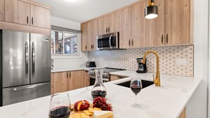 A modern kitchen with wooden cabinets, stainless steel appliances, a marble countertop, and a wine glass.