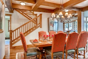 Un coin repas agrémenté d’un escalier en bois, de chaises à revêtement rouge, d’un lustre et d’une table à manger dressée pour six personnes.