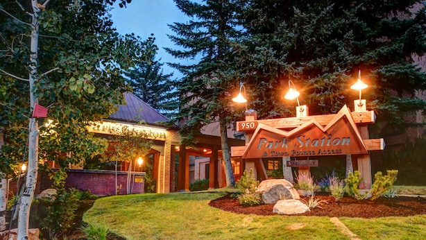 A park station with a wooden sign, a brick building, and a well-maintained garden. - Park Station 227 2 Bedroom Condo by RedAwning (Park City)