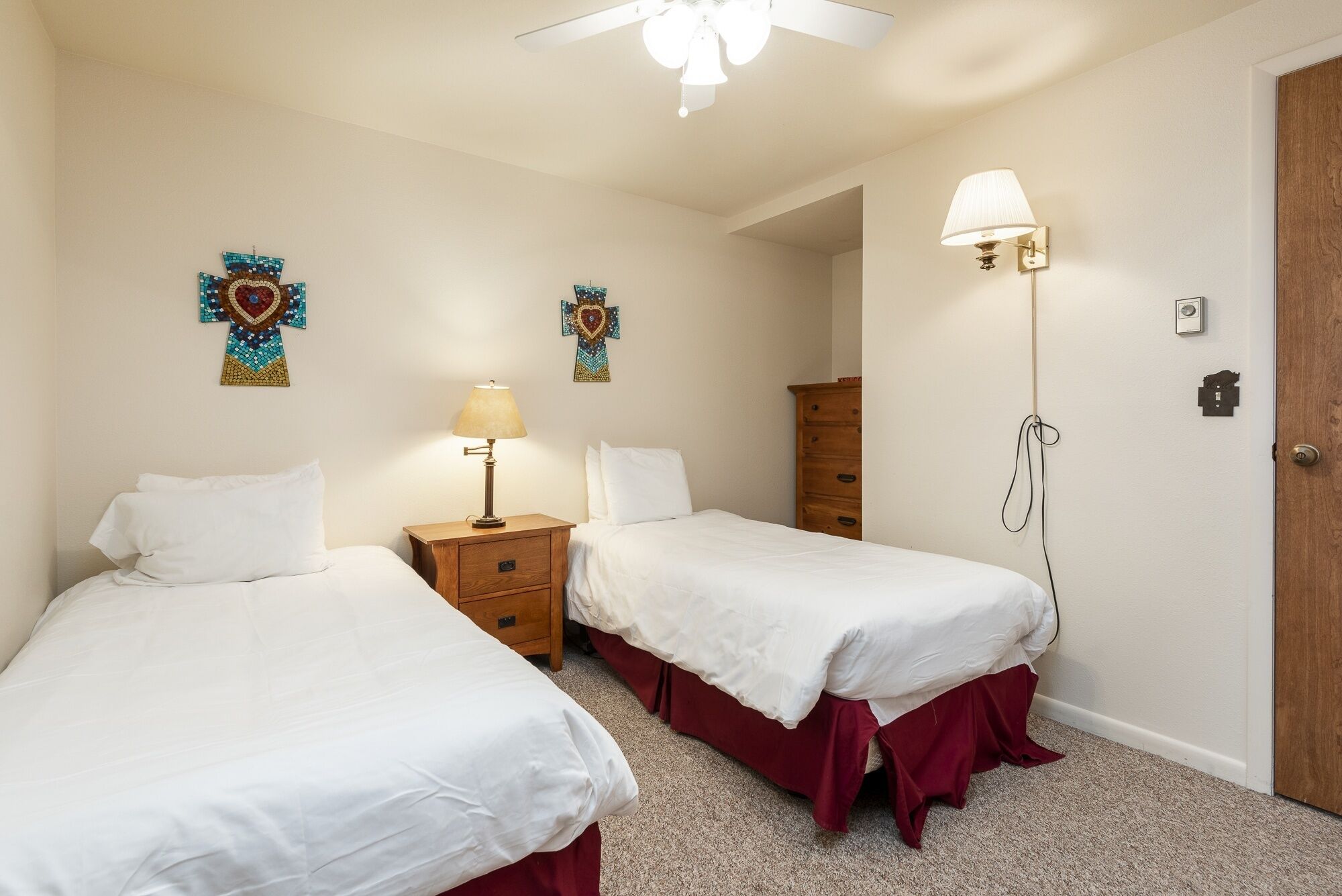 A hotel room with two single beds, a wooden nightstand with a lamp, a wooden dresser, and a door with a lock.