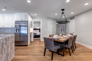 A modern kitchen with a stainless steel refrigerator, a marble countertop, and a wooden dining table with chairs. - Silver Cliff Village 103 2 Bedroom Condo by RedAwning (Park City)
