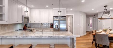 A modern kitchen with white cabinets, stainless steel appliances, and a marble island with bar stools.