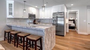Una cocina moderna con armarios blancos, una isla de mármol, electrodomésticos de acero inoxidable y taburetes de madera.