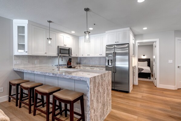 A modern kitchen with white cabinets, a marble island, stainless steel appliances, and wooden bar stools.