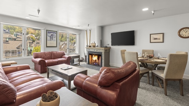 A modern living room with leather sofas, a fireplace, a dining area, and large windows offering a view of the outside. - Fashion Coalition 402 2 Bedroom Condo by RedAwning (Park City)