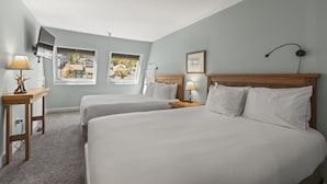 A hotel room with two beds, a desk, a lamp, a picture frame, and a window with a view of houses. - Fashion Coalition 402 2 Bedroom Condo by RedAwning (Park City)