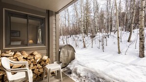 A covered porch with a stack of firewood, a metal grill, and a white plastic chair. - Snow Flower 135 2 Bedroom Condo by RedAwning (Park City)
