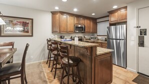 A kitchen with wooden cabinets, a stainless steel refrigerator, a microwave, and a granite countertop. - Snow Flower 135 2 Bedroom Condo by RedAwning (Park City)