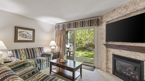 A living room with a fireplace, patterned sofa, and a television. - Snow Flower 135 2 Bedroom Condo by RedAwning (Park City)