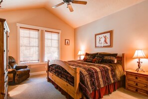 Cozy bed with a wooden headboard, flanked by bedside lamps, and a large window with blinds.
