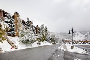 A snow-covered street with a building on the left and a mountain in the background.