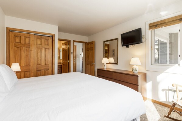 A bedroom with a large bed, wooden wardrobe, dresser, and a mounted TV.