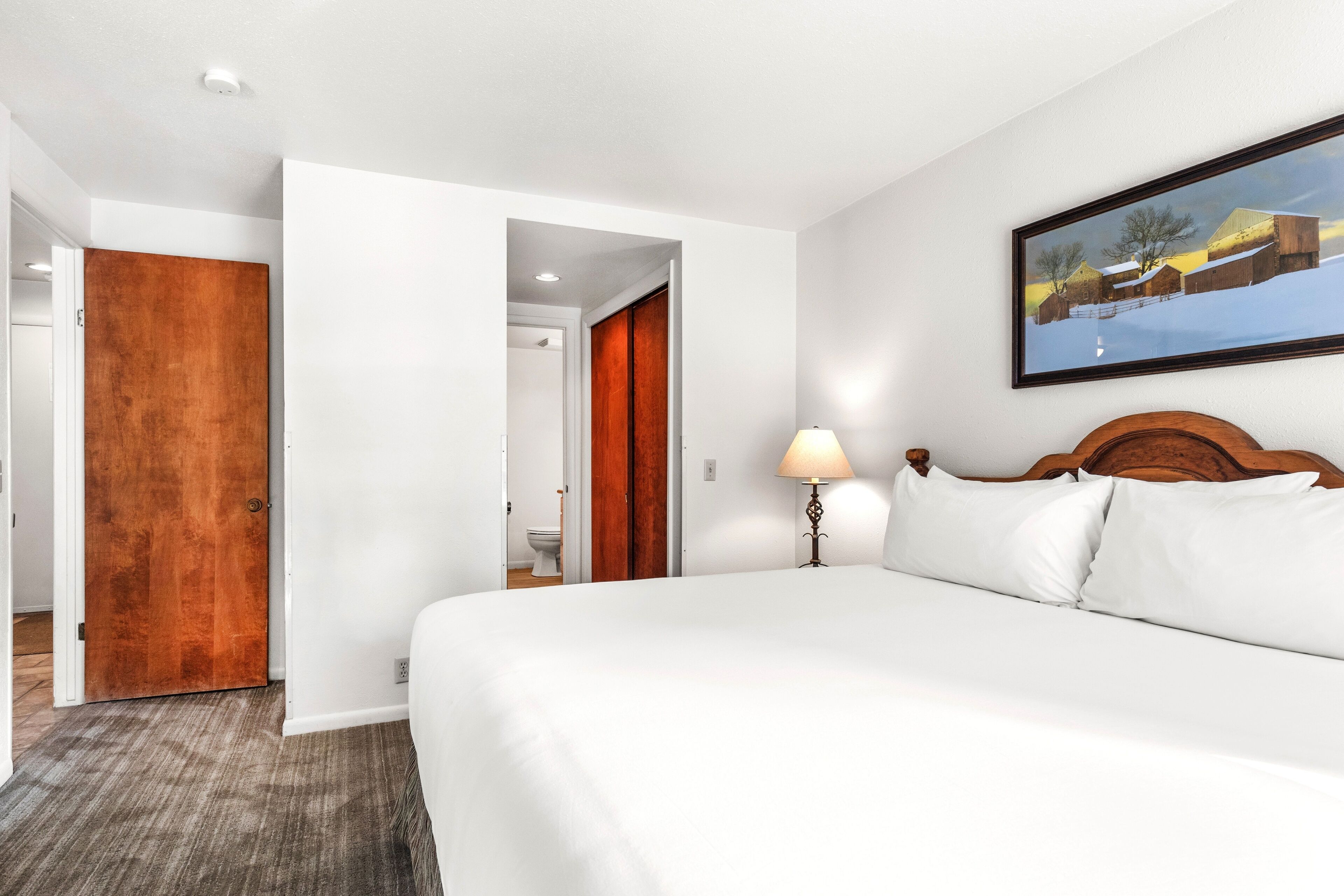 A hotel room with a large bed, a wooden door, and a painting on the wall.