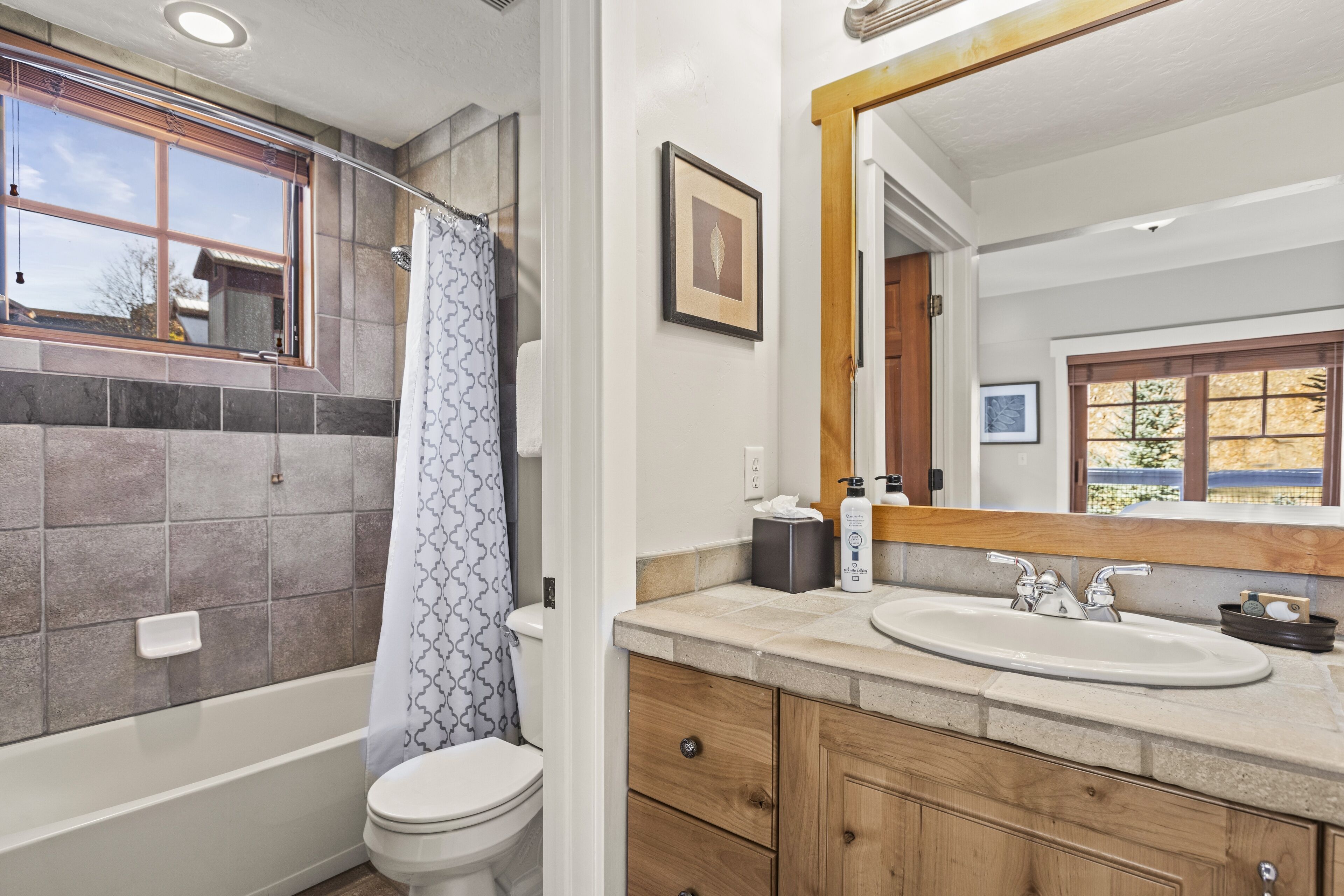 A bathroom with a bathtub, toilet, vanity with a sink, and a large mirror.